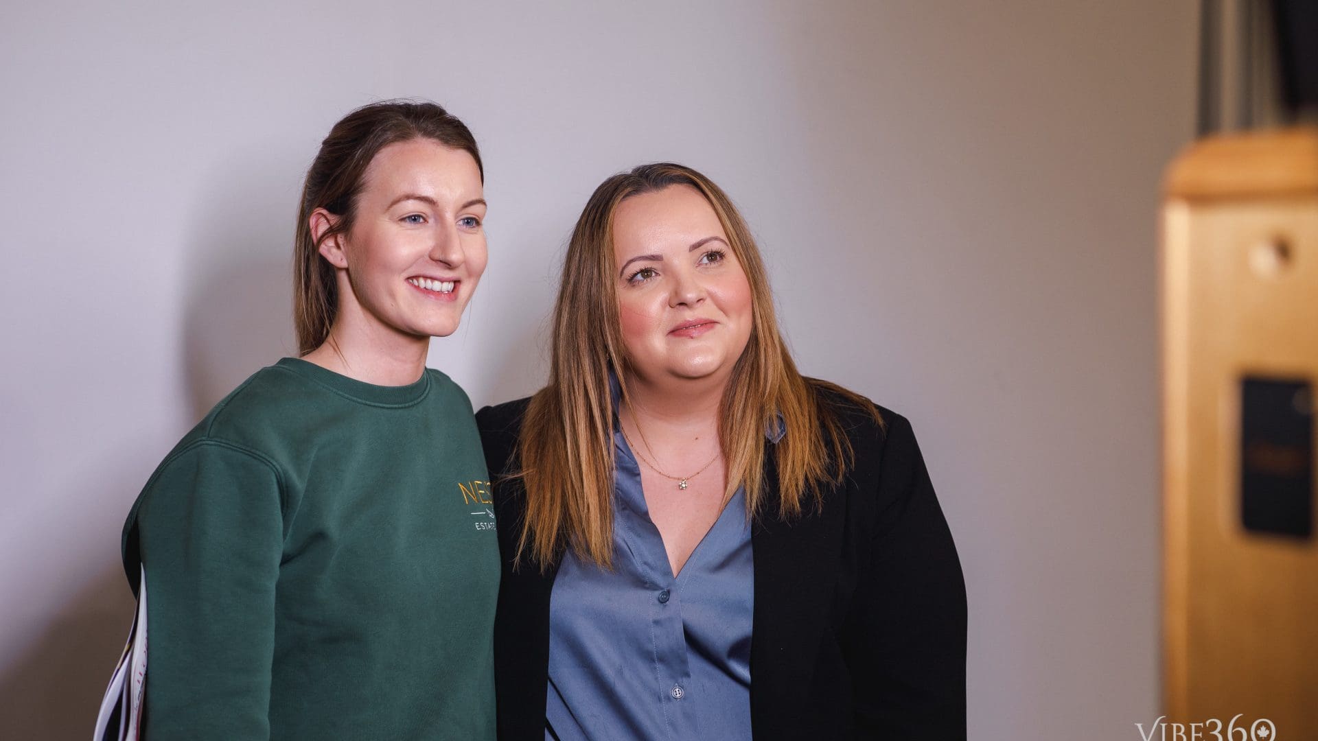 Two women smiling for a photo in casual and business attire at an event.