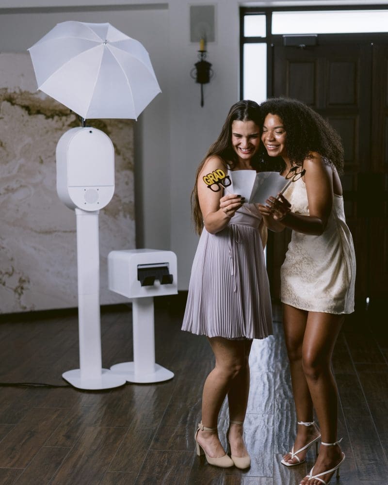 Two friends celebrating graduation with a photo booth session, holding Grad props and smiling.