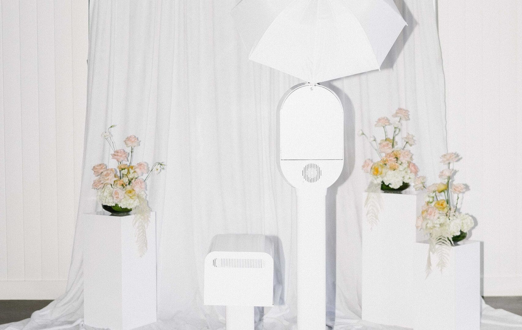 Elegant photo booth setup with white umbrella and floral decor against a draped curtain background.